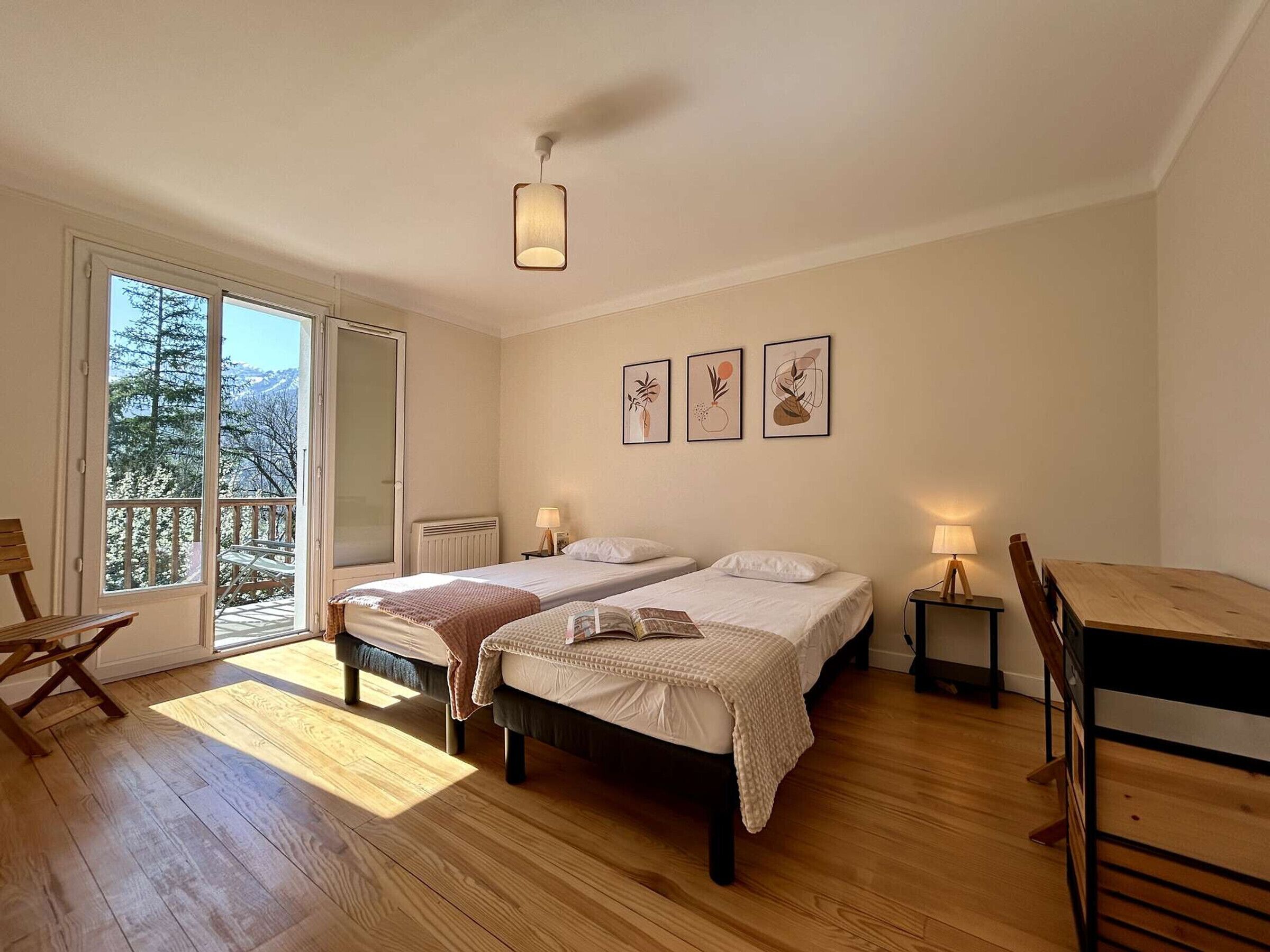 Een slaapkamer met twee bedden, een houten vloer, een balkon met uitzicht en een eettafel.
