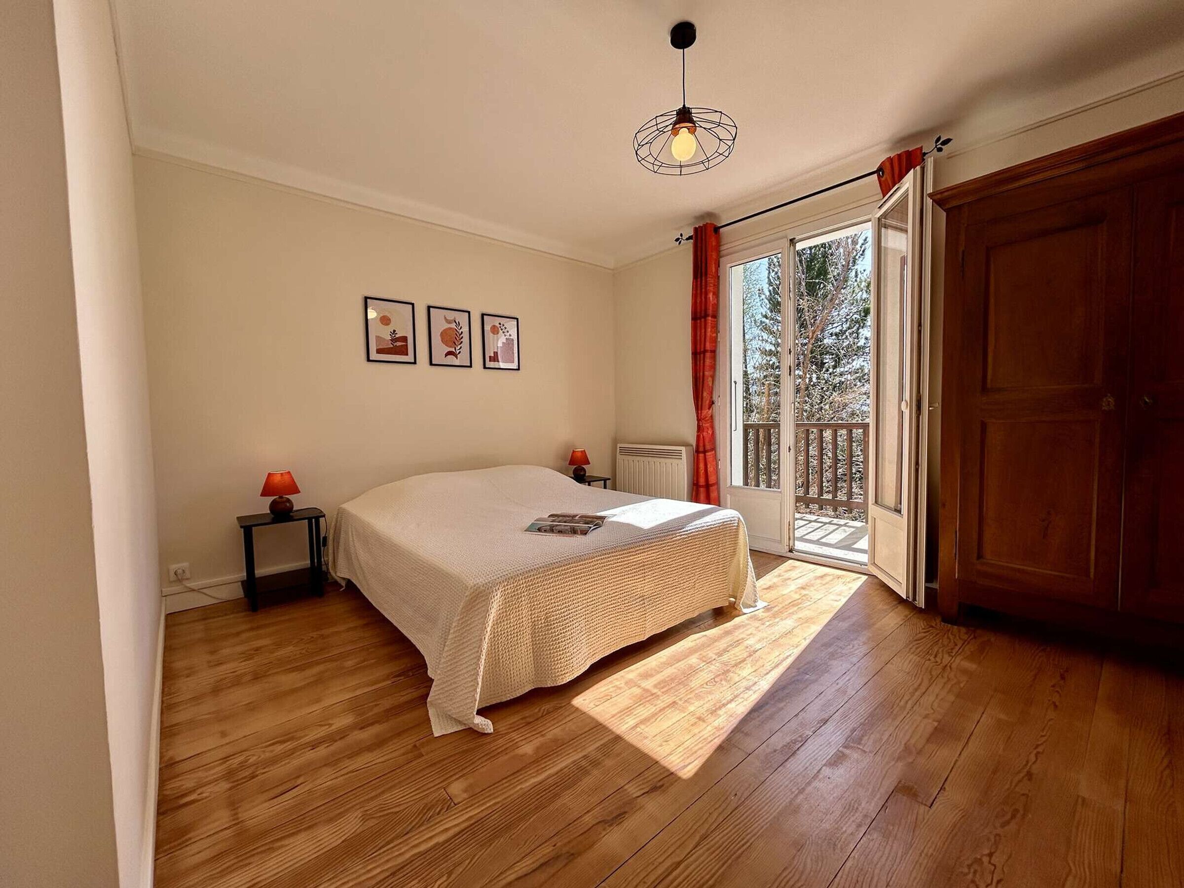 A bedroom with a bed, a nightstand, a radiator, a window with curtains, and a door leading to a balcony.