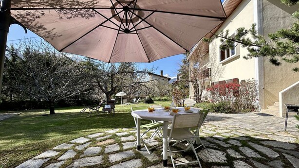 A patio with a table and chairs under a large umbrella, surrounded by stone tiles and greenery. - Spacious 4-Room Apartment with Garden & Parking - Sleeps 6, Briançon (Briançon)