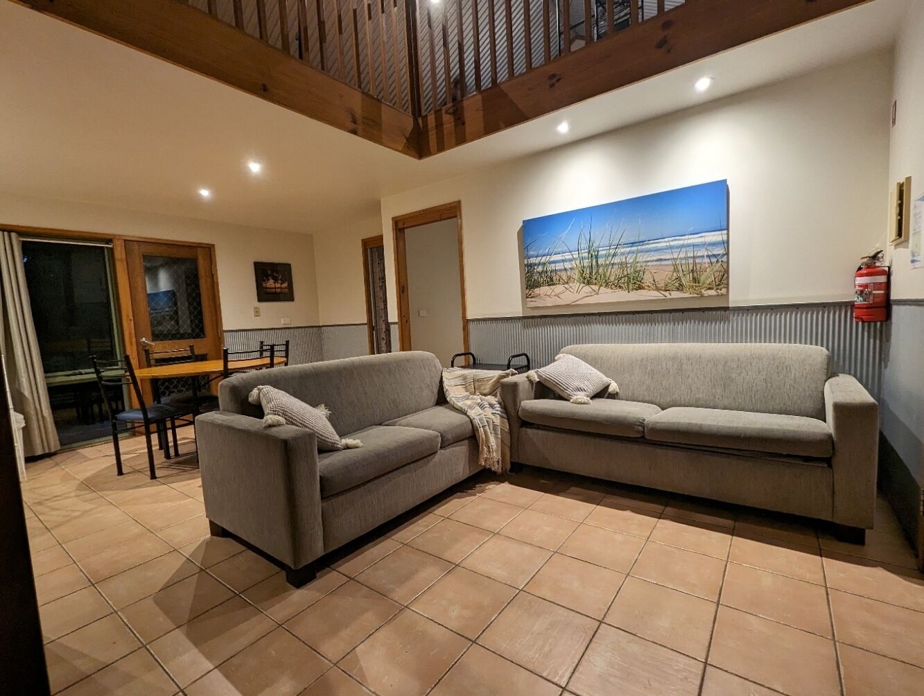 Ein Wohnzimmer mit zwei Sofas, einem Esstisch, Stühlen, einem Bild an der Wand und einem Feuerlöscher.