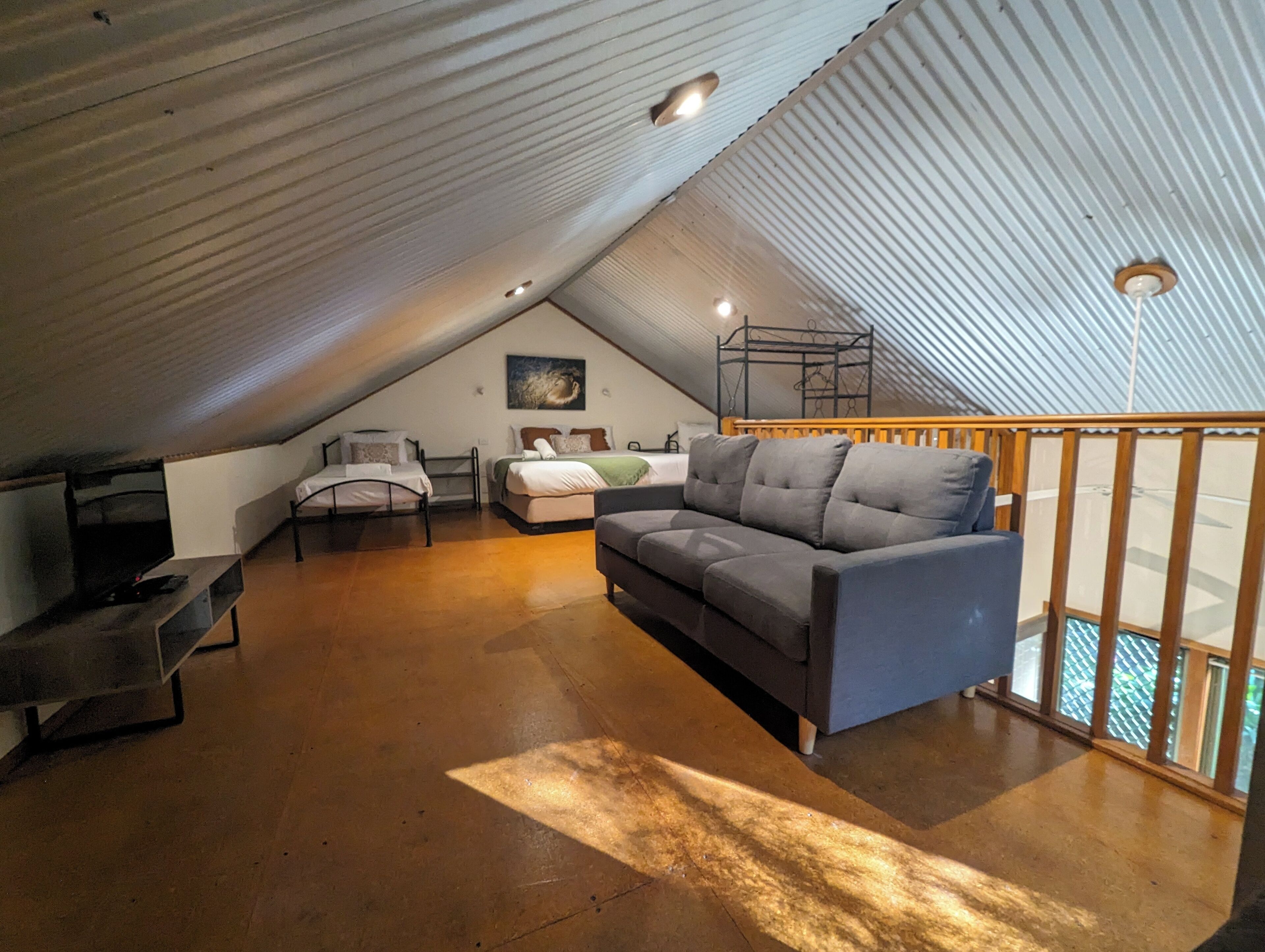 A cozy attic bedroom with a loft bed, a sofa, and a TV.
