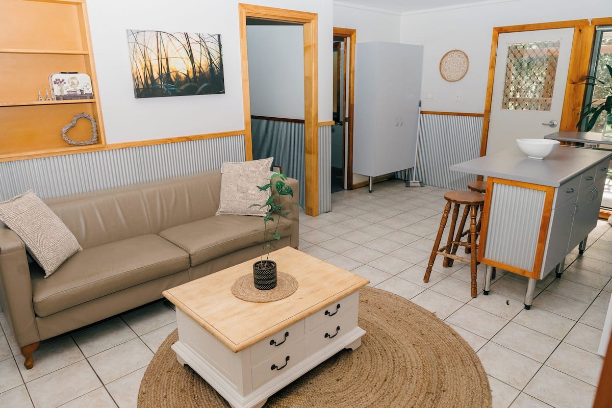 Ein kompakter Wohnraum mit einer Couch, einem kleinen Holztischchen, einer Küchenzeile mit einem Hocker und einem Schrank.