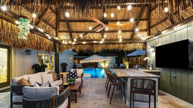 An outdoor living area with a thatched ceiling, a pool, and a bar area.