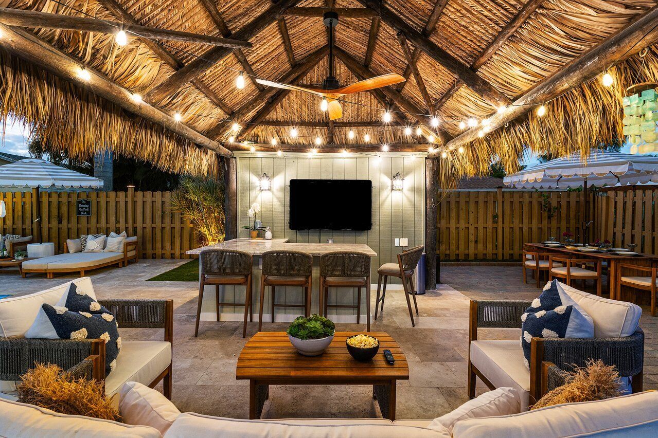An outdoor patio with a thatched roof, wooden furniture, and a flat-screen TV.