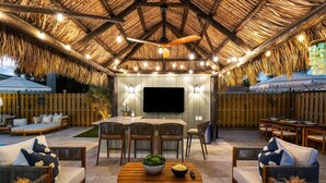 An outdoor patio with a thatched roof, wooden furniture, and a flat-screen TV.