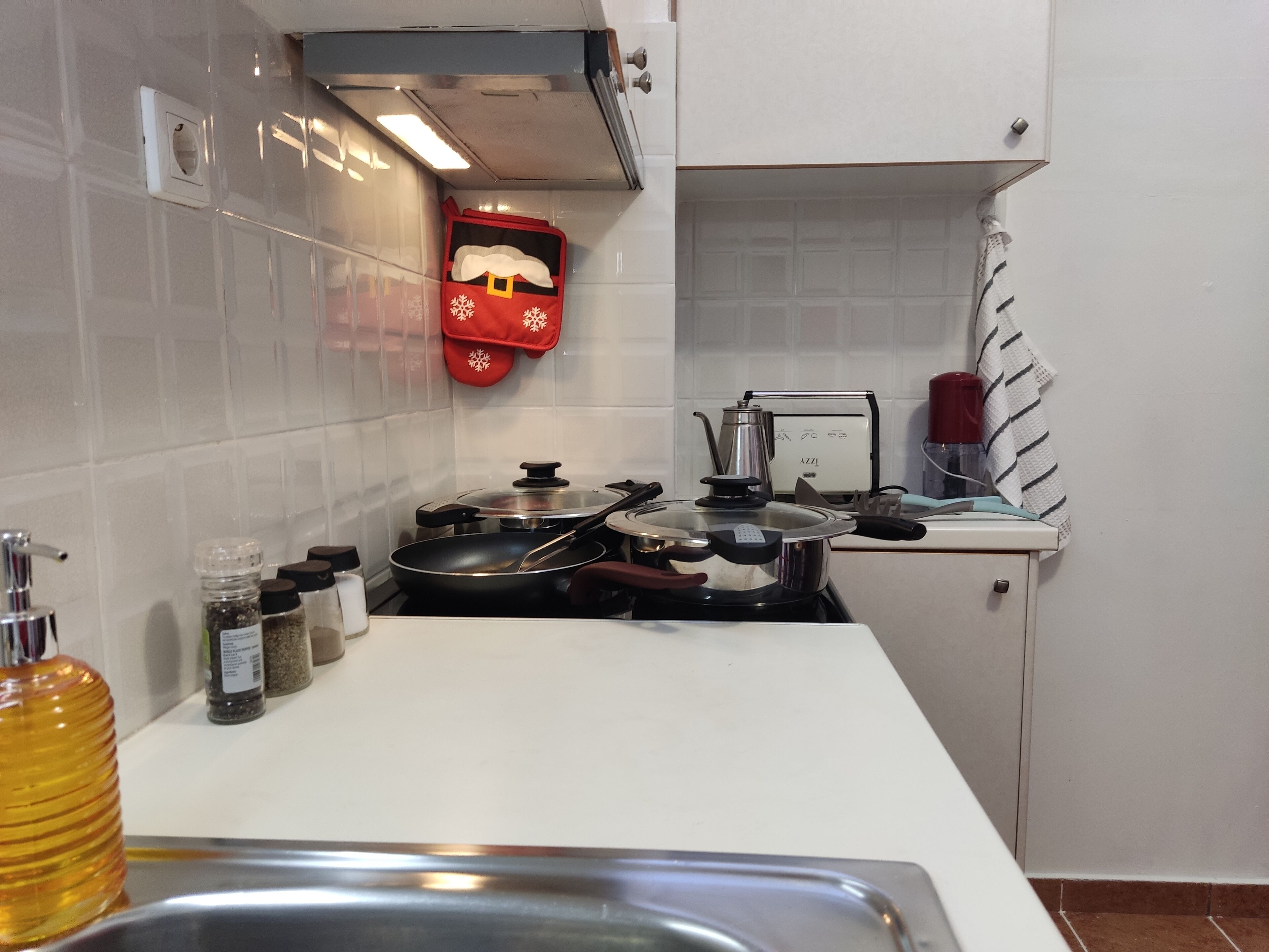 Una cucina con un fornello, pentole, un bollitore e un forno a microonde. Sul bancone ci sono barattoli di spezie e una bottiglia d'olio.