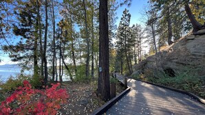 A wooden boardwalk through a forested area with a rocky outcrop on the right and a body of water in the background.