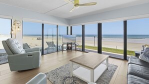 Una sala de estar moderna con un ventanal a la playa, un ventilador de techo y un televisor de pantalla plana.