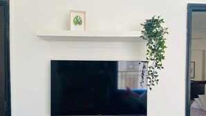 Ein Flachbildfernseher an einer weißen Wand, darunter ein Regal.