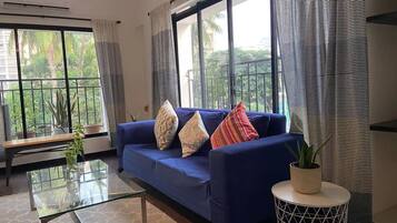 A living room with a blue sofa, a glass coffee table, and a potted plant.
