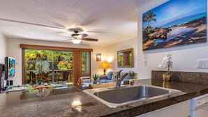 A modern kitchen with granite countertops, a stainless steel sink, and a ceiling fan.
