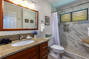 A bathroom with a granite countertop sink, a large mirror, a toilet, and a shower with a curtain. - Spacious design with stunning wood floors (Kihei)
