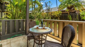 A covered outdoor area with a round glass table, wicker chairs, and a wooden fence.