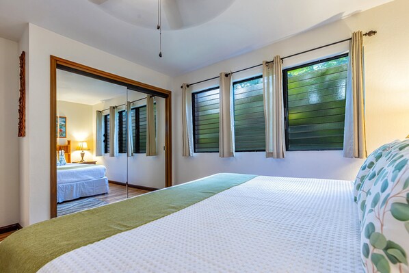 A bedroom with a large bed, a mirror, a window with curtains, and a view of another room. - Spacious design with stunning wood floors (Kihei)