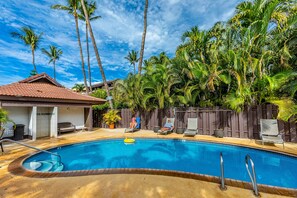 A swimming pool with a tiled deck, surrounded by palm trees and a wooden fence. - Spacious design with stunning wood floors (Kihei)