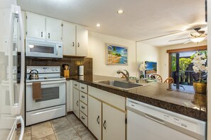A kitchen with white cabinets, a microwave, stove, and dishwasher. There is a painting of a beach scene on the wall. - Spacious design with stunning wood floors (Kihei)