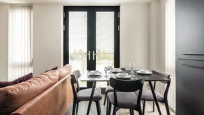 Un espace repas moderne avec une table dressée pour quatre personnes, un canapé et un réfrigérateur de couleur sombre.