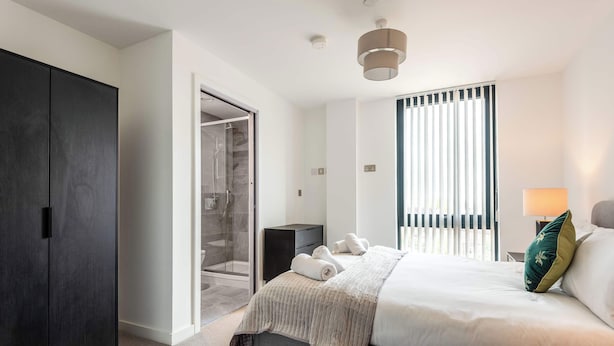Une chambre d’hôtel moderne dotée d’un grand lit, d’un dressing, d’une douche et offrant une vue sur l’extérieur par la fenêtre.