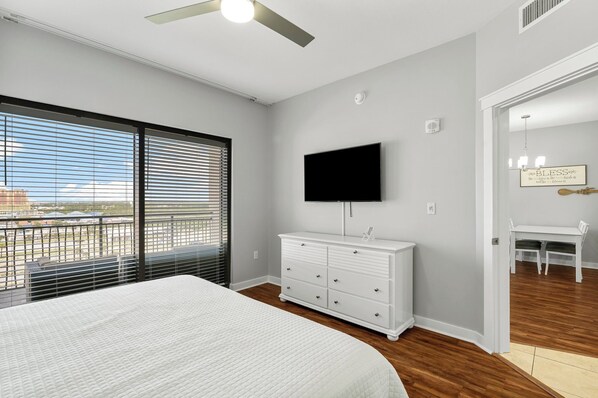 Un dormitorio con cama, cómoda blanca, televisor de pantalla plana y balcón con persianas.