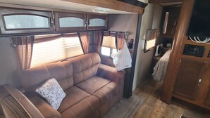 Ein gemütliches Wohnmobil-Interieur mit einer braunen Ledersitzgruppe, einer kleinen Küchenzeile und einem Fenster mit Vorhängen.