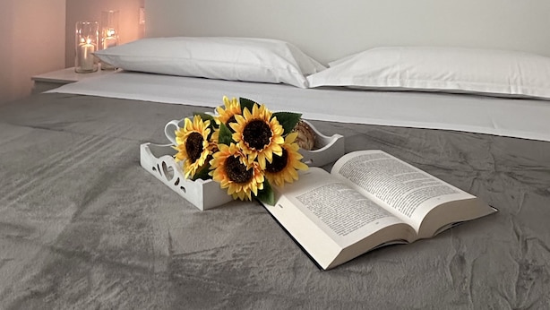 Une chambre à coucher comprenant un lit, une œuvre d’art murale composée de plusieurs panneaux représentant des corps célestes, une table de chevet avec des bougies et un vase décoratif contenant des tournesols.