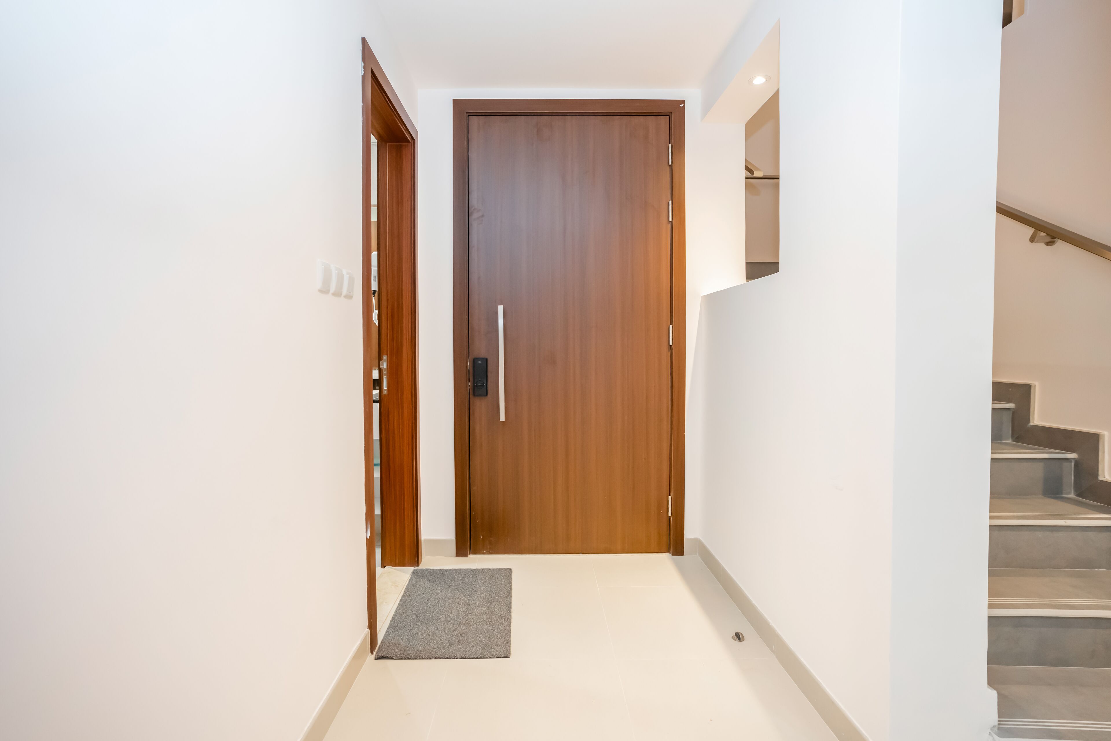 Un pasillo con puerta de madera, un tapete pequeño y una escalera.