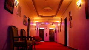 Un couloir avec un tapis rouge, des chaises en bois et des luminaires fixés au mur.