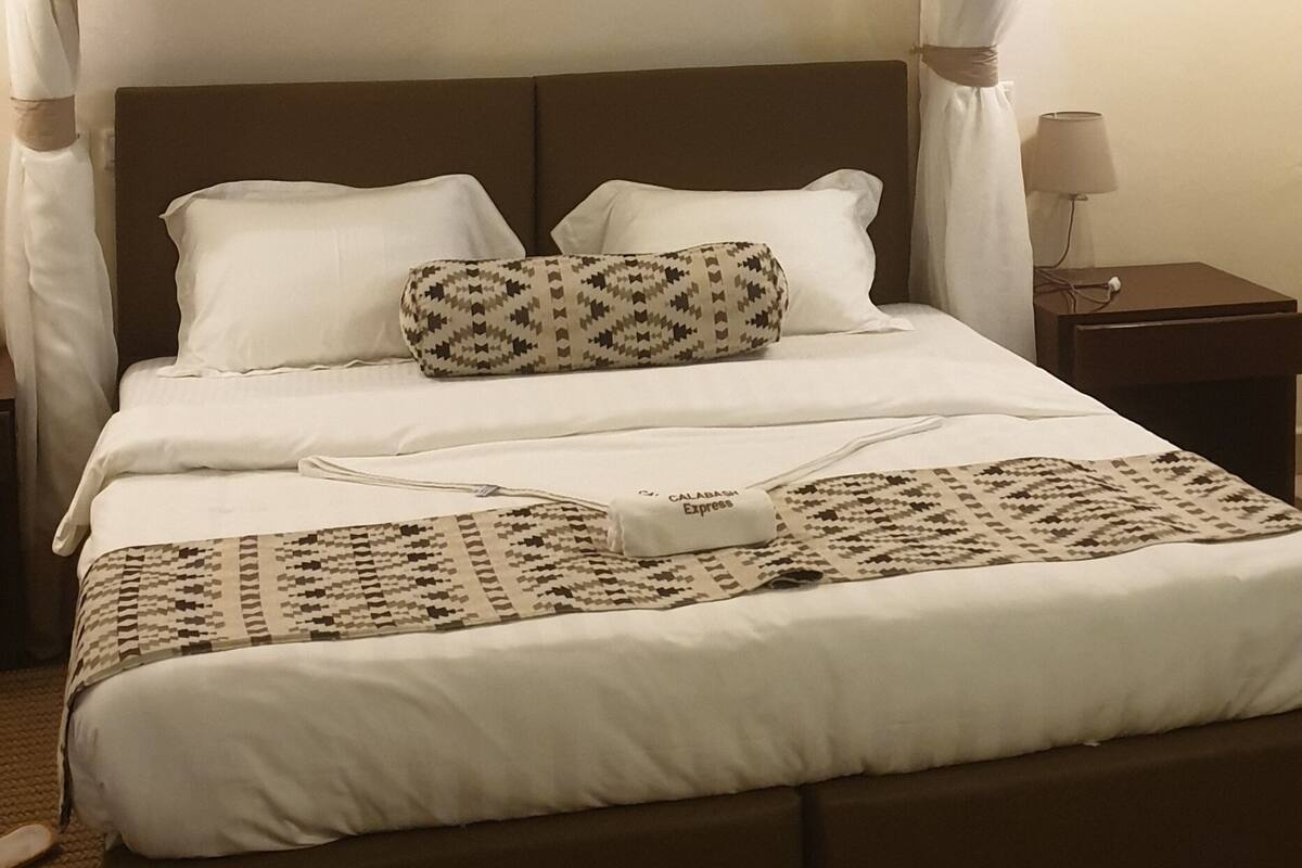 Un letto rifatto con cura, con una coperta a motivi e un comodino con lampada.