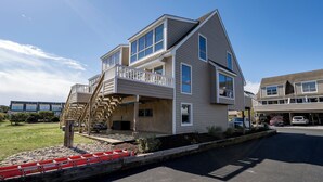 A two-story house with a balcony, a staircase, and a driveway with cars.