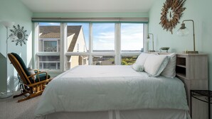 A bedroom with a large bed, a rocking chair, a view of the outside, and a decorative wall piece.