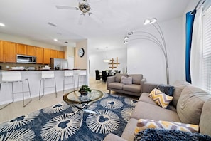 A modern living room with a sofa, coffee table, and a dining area with chairs. - Pool Oasis 4BR Townhome w Theme rooms near Disney (Kissimmee)