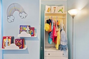 Une chambre d’enfant décorée aux couleurs de l’arc-en-ciel, avec des étagères remplies de livres, un portant à vêtements aux couleurs vives et une lampe.