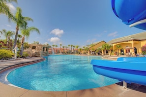 Une piscine avec un toboggan, des palmiers et des bâtiments d’un complexe hôtelier.