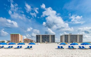 Una playa con tumbonas y sombrillas, un edificio de hotel y otro edificio al fondo.
