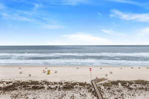 Ein Strand mit einer Holzpromenade, die zum Meer führt, Sanddünen und einem klaren Himmel.