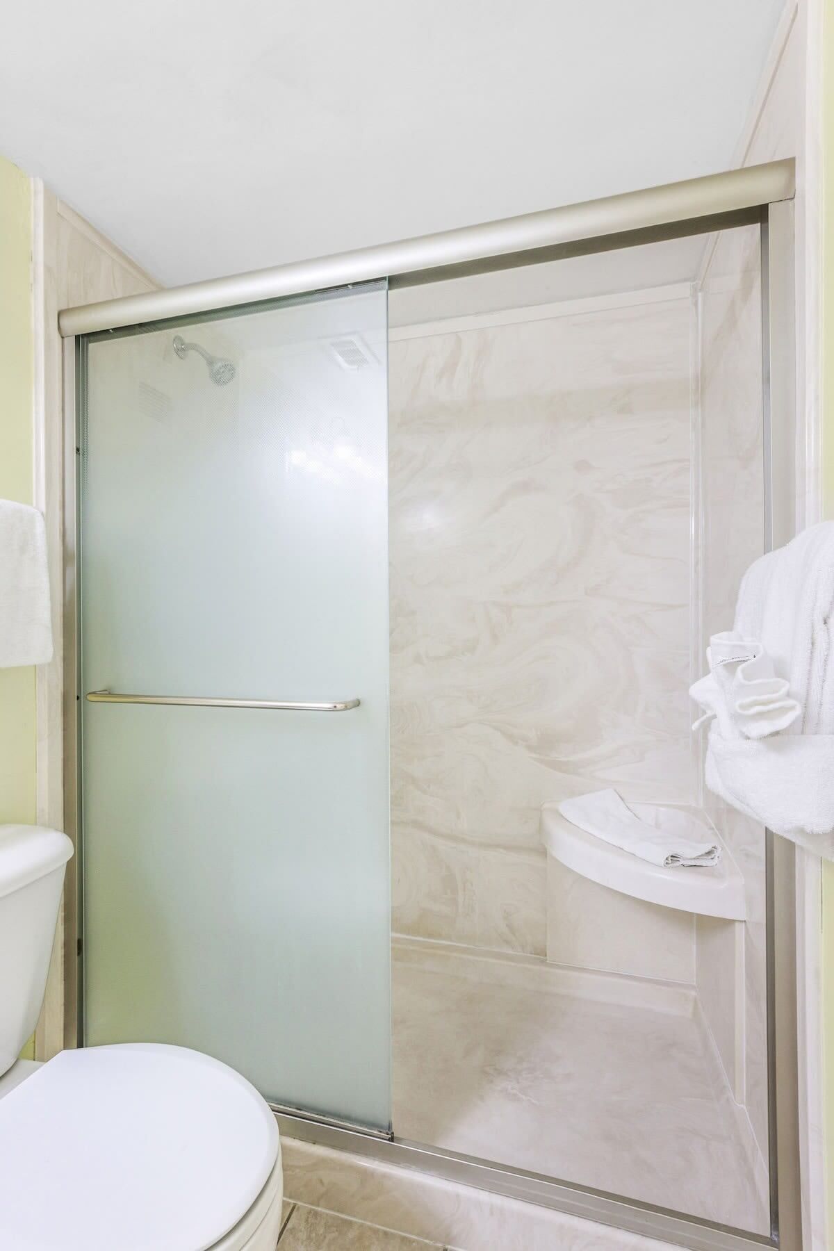 A bathroom with a glass-enclosed shower, a toilet, and a sink with a towel.