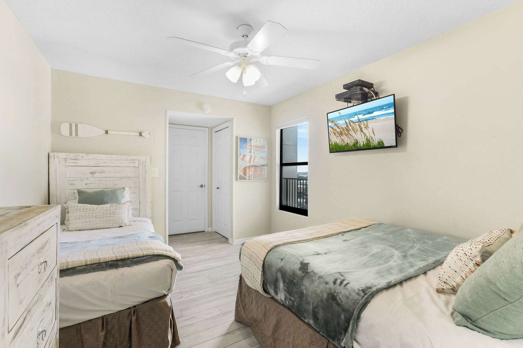 A bedroom with two beds, a ceiling fan, a TV, and a door leading to another room.