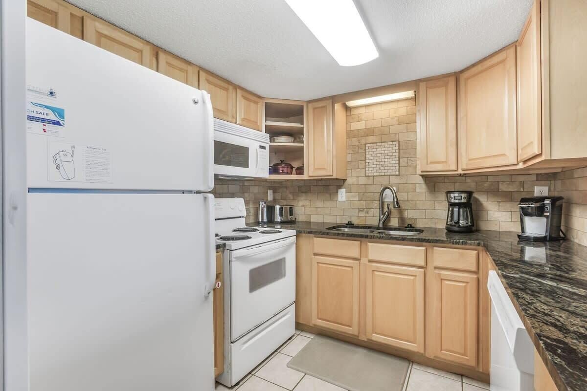 A kitchen with wooden cabinets, a white refrigerator, a stove, a microwave, and a coffee maker.