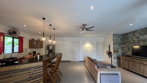 A modern kitchen with a central island, wooden chairs, and a ceiling fan.