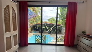 A room with a sliding glass door leading to a pool area, a white wardrobe, and a small table with a plant.