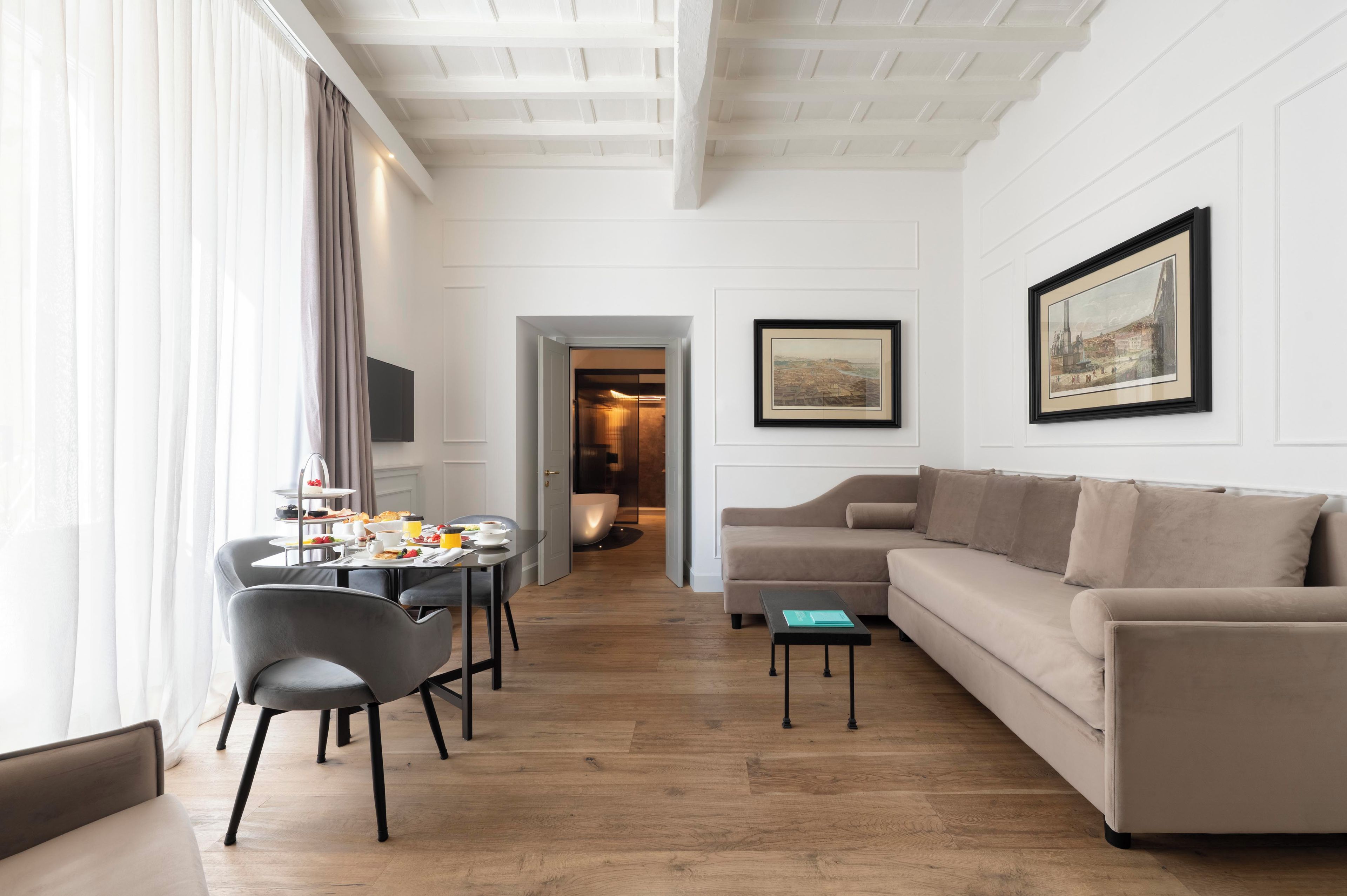 A modern living room with a sofa, a dining table with chairs, and artwork on the walls.