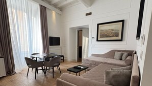 A spacious living room with a large beige sofa, a dining table with chairs, and a flat-screen TV mounted on the wall. - Palazzo Goldoni Condotti Collection (Rome)