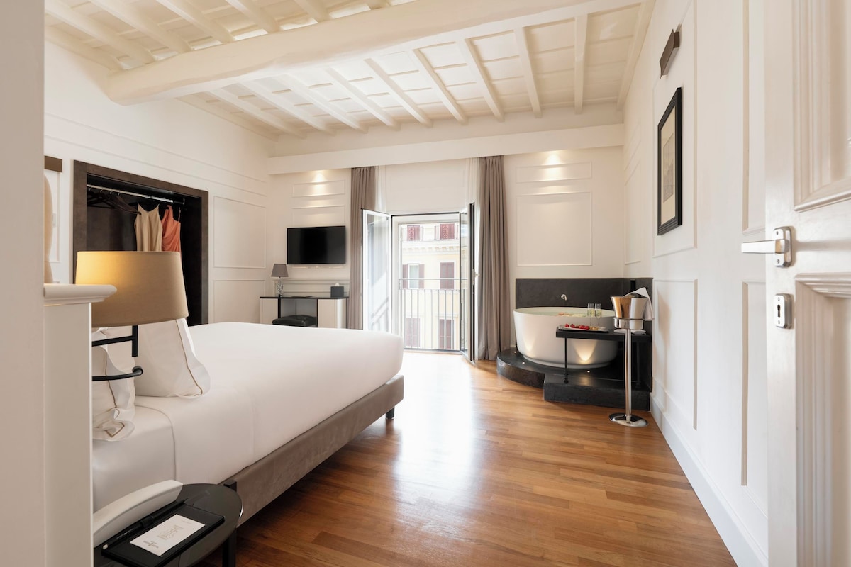 A hotel room with a bed, bedside table, lamp, wardrobe, TV, and a bathroom with a bathtub and sink.