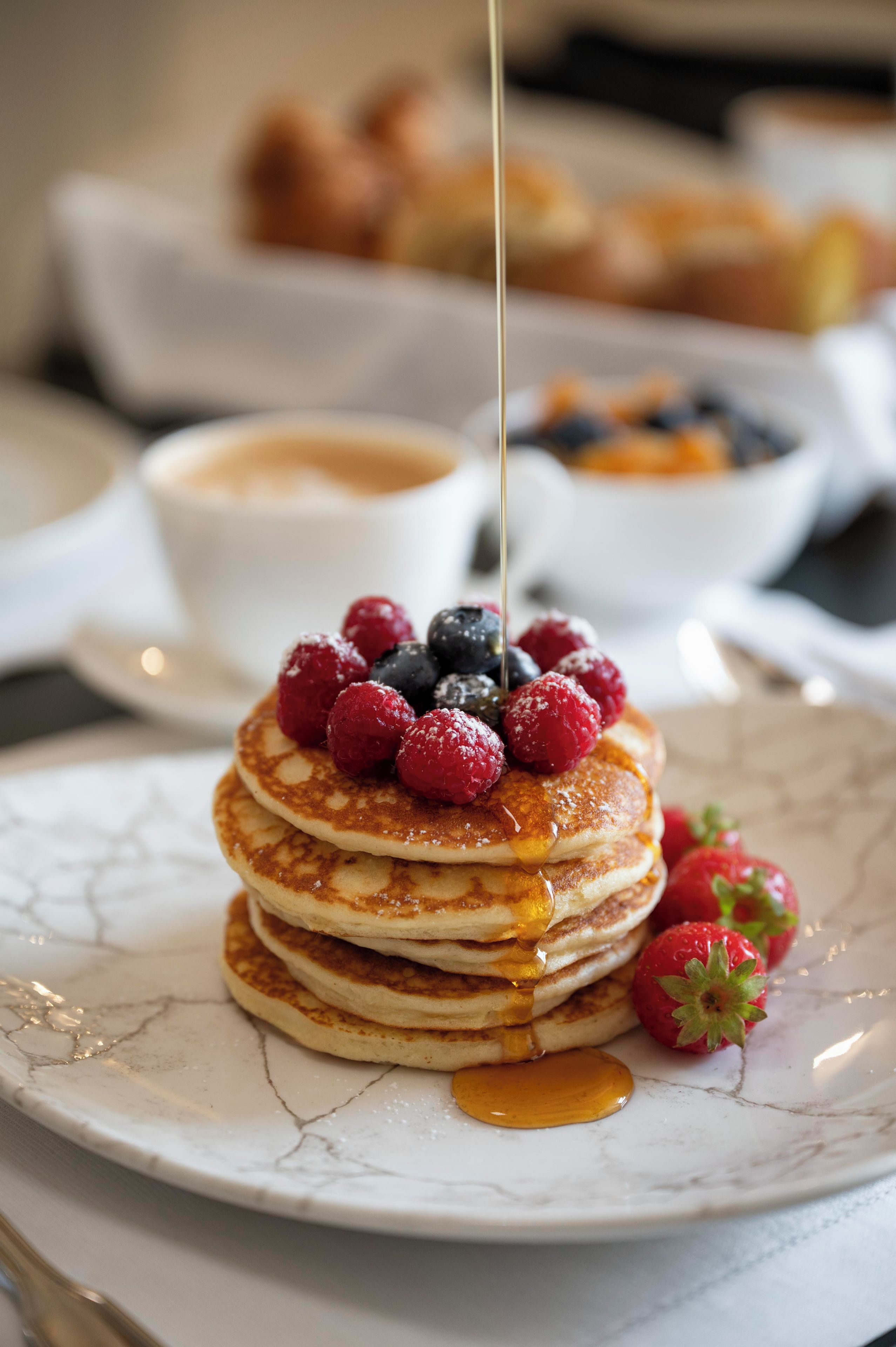 Ein Stapel Pfannkuchen mit Beeren und Sirup auf einem Teller.