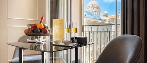 A room with a dining table set for two, a fruit bowl, a bottle of champagne, and a menu.