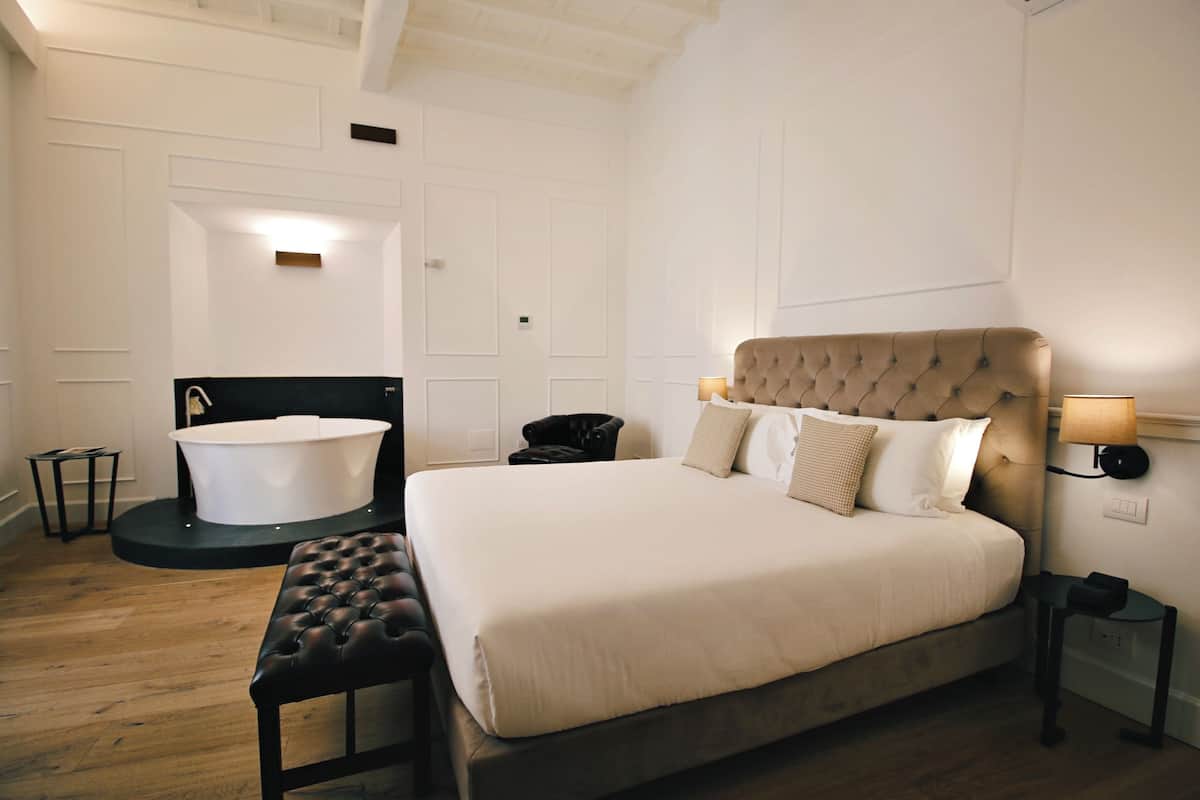 A bedroom with a large bed, a round bathtub, a bench, and a small table.
