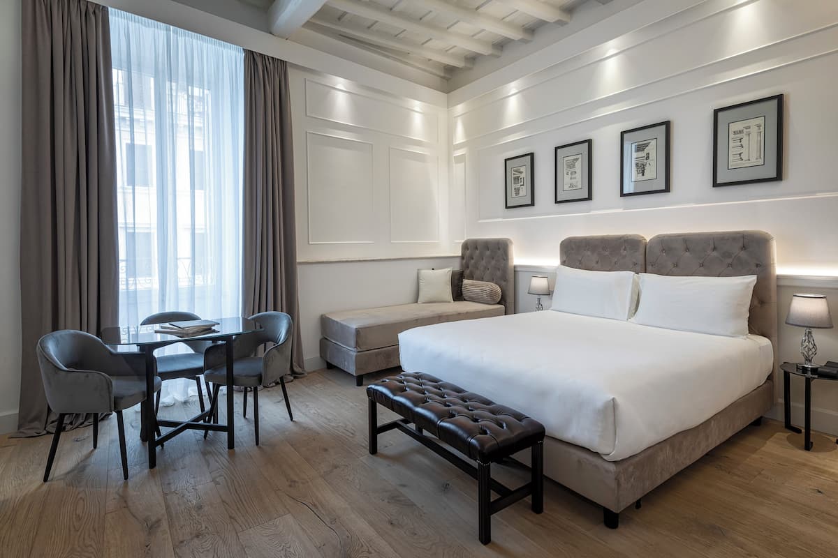 A hotel room with a large bed, a desk with chairs, a bench, and a sofa.