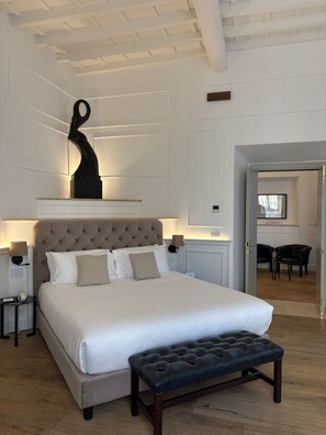 A modern bedroom with a large bed, a tufted headboard, bedside lamps, and a black sculpture on the wall. - Palazzo Goldoni Condotti Collection (Rome)