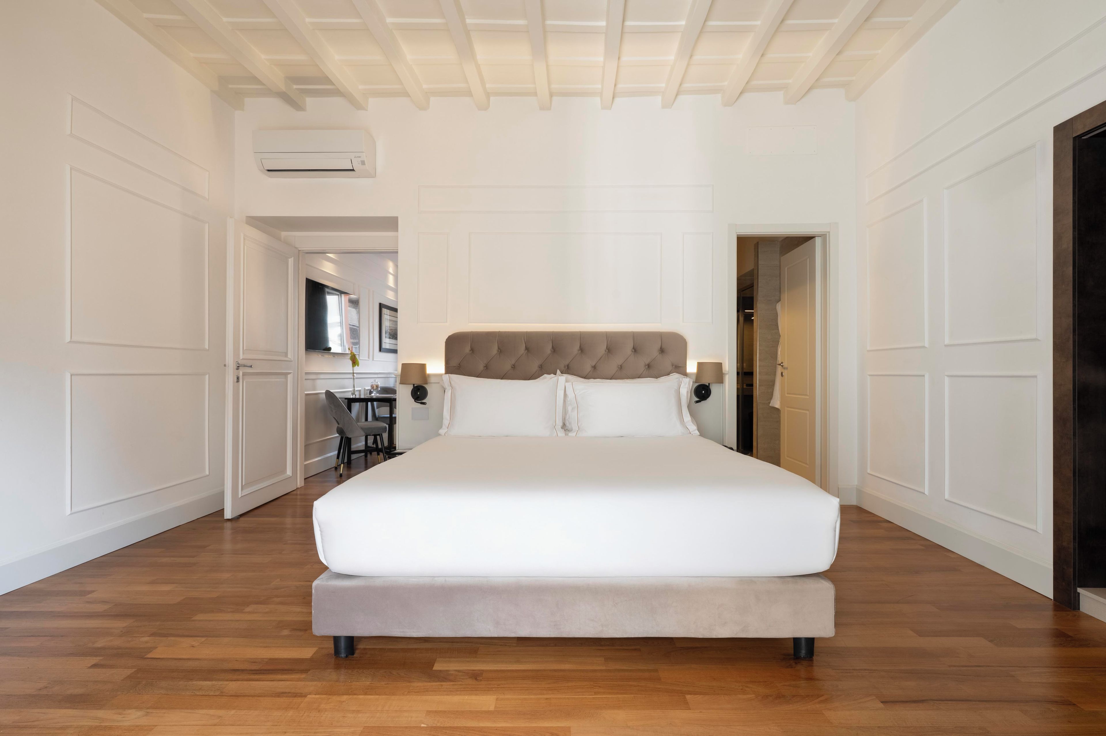 Une chambre spacieuse avec un grand lit, un plancher en bois et un plafond avec des poutres apparentes.