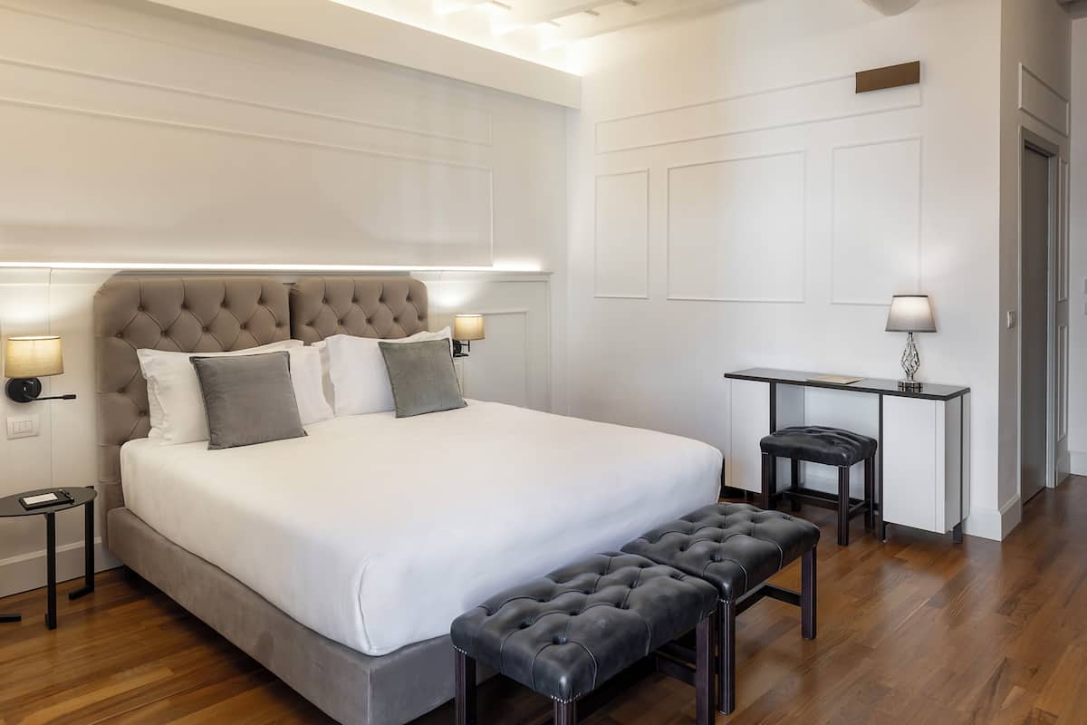 A modern bedroom with a large bed, bedside tables, a desk, and a bench.